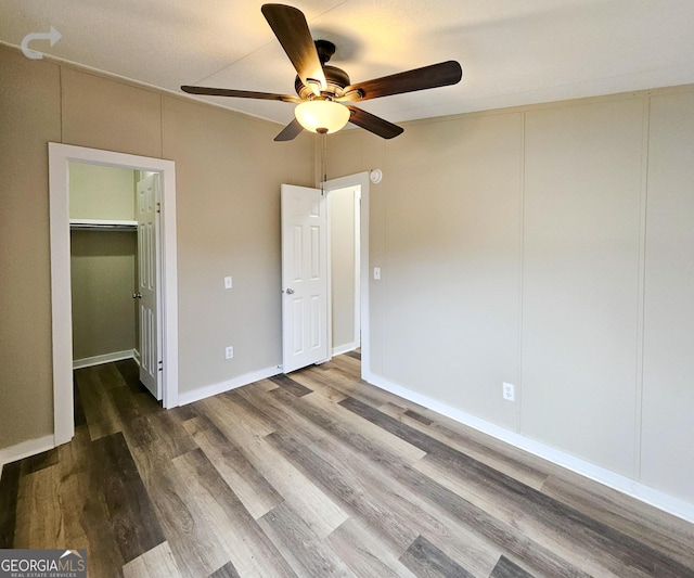 unfurnished bedroom featuring ceiling fan, a spacious closet, hardwood / wood-style floors, and a closet