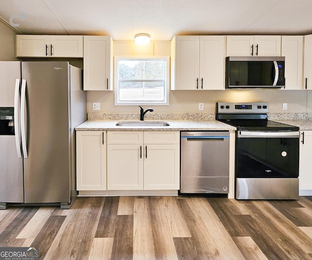 kitchen with sink, white cabinets, hardwood / wood-style flooring, stainless steel appliances, and a textured ceiling