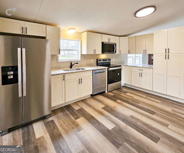 kitchen with appliances with stainless steel finishes, sink, lofted ceiling, and light hardwood / wood-style floors