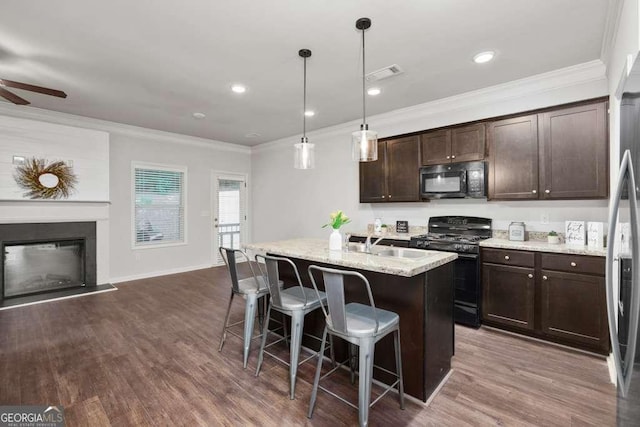 kitchen with a breakfast bar, hanging light fixtures, light stone counters, black appliances, and a center island with sink