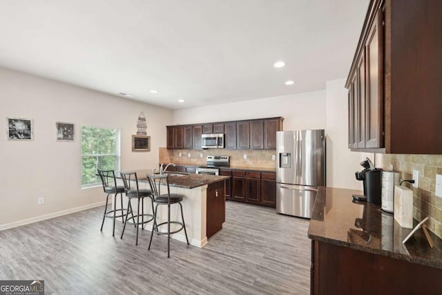 kitchen featuring appliances with stainless steel finishes, an island with sink, sink, dark stone countertops, and light hardwood / wood-style floors