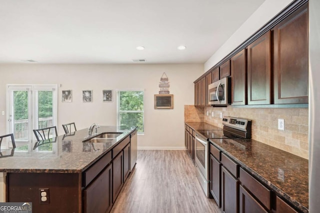 kitchen featuring sink, tasteful backsplash, dark stone counters, stainless steel appliances, and a kitchen island with sink