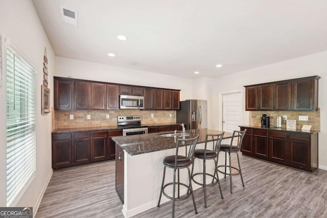 kitchen with a breakfast bar, sink, light wood-type flooring, stainless steel appliances, and a kitchen island with sink