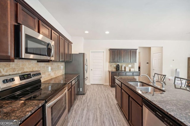 kitchen with appliances with stainless steel finishes, sink, dark stone counters, dark brown cabinetry, and light wood-type flooring