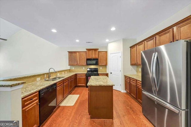 kitchen featuring sink, light stone counters, kitchen peninsula, a kitchen island, and black appliances