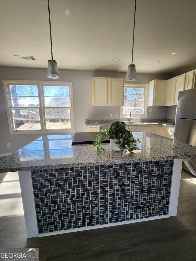 kitchen with hanging light fixtures, stainless steel fridge, light stone countertops, and a kitchen island