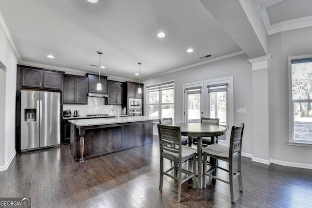 kitchen with pendant lighting, a kitchen bar, stainless steel appliances, plenty of natural light, and a center island with sink