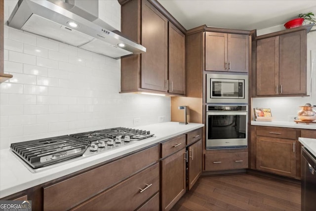 kitchen with wall chimney exhaust hood, stainless steel appliances, dark wood-type flooring, and backsplash