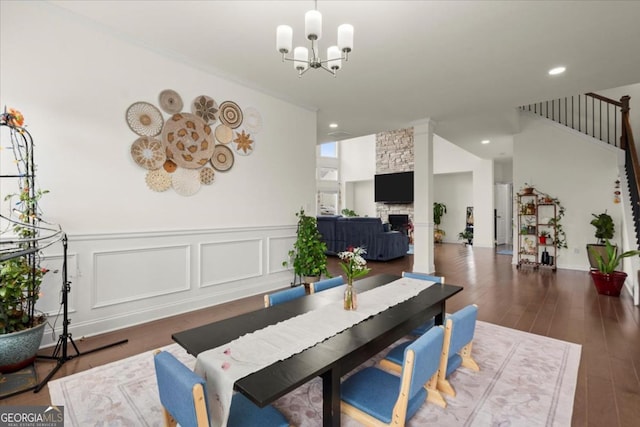 dining room with dark hardwood / wood-style floors, a stone fireplace, and an inviting chandelier