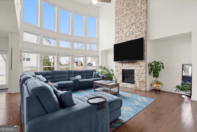 living room featuring a stone fireplace, a towering ceiling, and dark hardwood / wood-style flooring