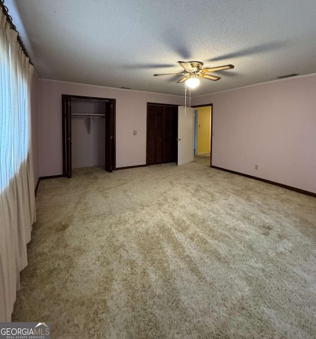 unfurnished bedroom featuring light carpet, multiple closets, a textured ceiling, and ceiling fan