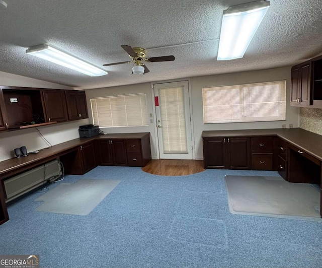 unfurnished office featuring built in desk, lofted ceiling, light colored carpet, ceiling fan, and a textured ceiling