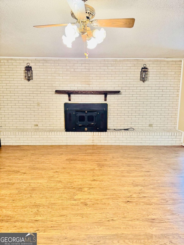 unfurnished living room featuring hardwood / wood-style flooring, ceiling fan, brick wall, and a textured ceiling