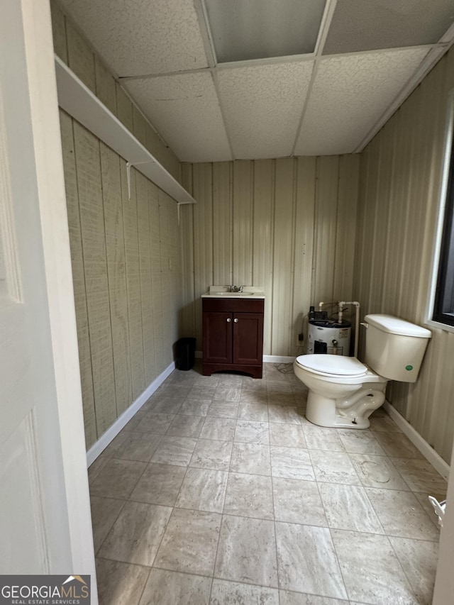 bathroom featuring a drop ceiling, vanity, toilet, and wood walls