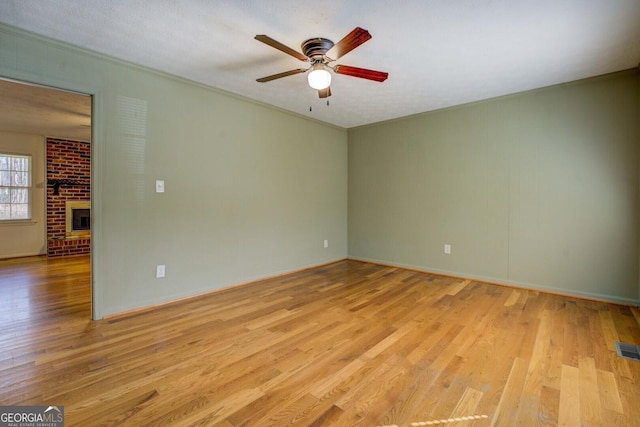 spare room featuring a brick fireplace, crown molding, light hardwood / wood-style floors, and ceiling fan