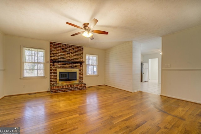 unfurnished living room with ceiling fan, a fireplace, a textured ceiling, and light wood-type flooring