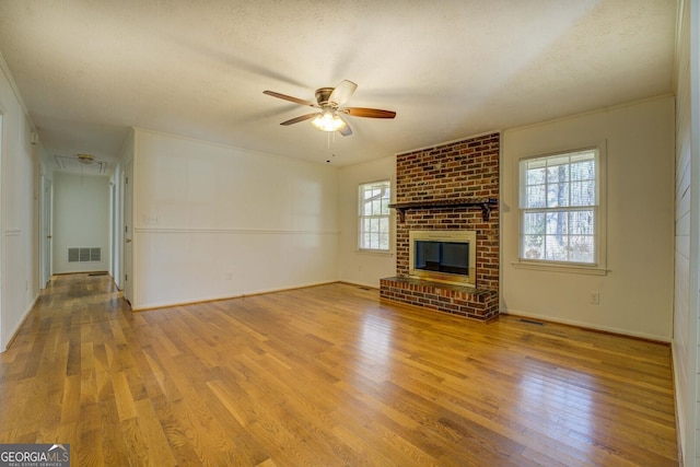 unfurnished living room with a textured ceiling, a fireplace, light hardwood / wood-style floors, and ceiling fan