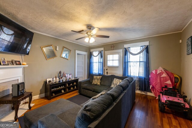 living area with baseboards, a fireplace with raised hearth, ornamental molding, dark wood-style flooring, and a textured ceiling