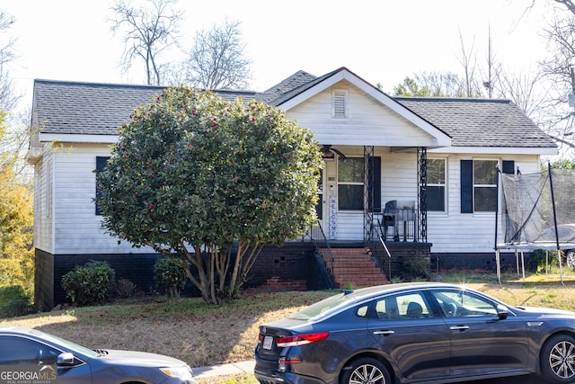 bungalow-style house featuring covered porch, a shingled roof, and a trampoline