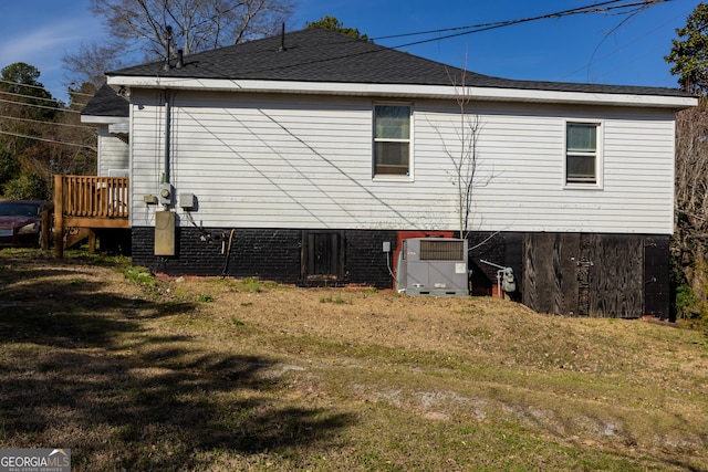 back of house with a wooden deck, central AC unit, a lawn, and roof with shingles