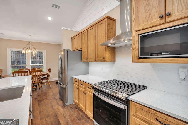 kitchen featuring crown molding, backsplash, appliances with stainless steel finishes, a sink, and wall chimney range hood