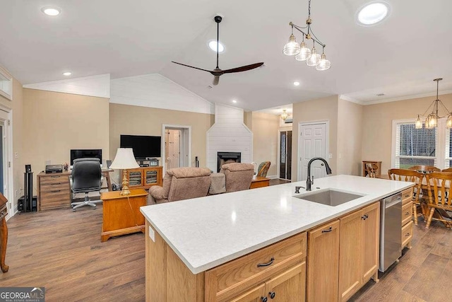 kitchen featuring a large fireplace, an island with sink, a sink, stainless steel dishwasher, and ceiling fan with notable chandelier