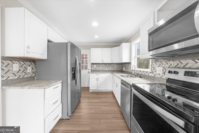 kitchen with appliances with stainless steel finishes, tasteful backsplash, sink, white cabinets, and ornamental molding