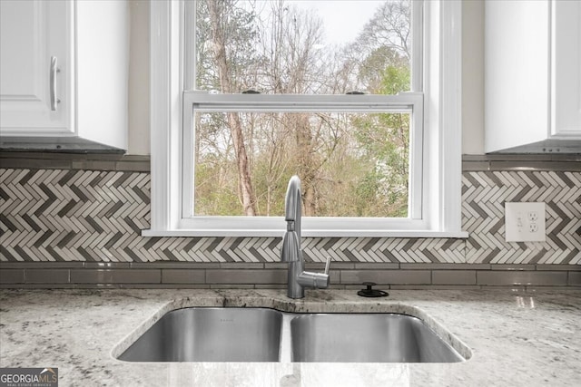 room details featuring white cabinetry, sink, light stone counters, and decorative backsplash