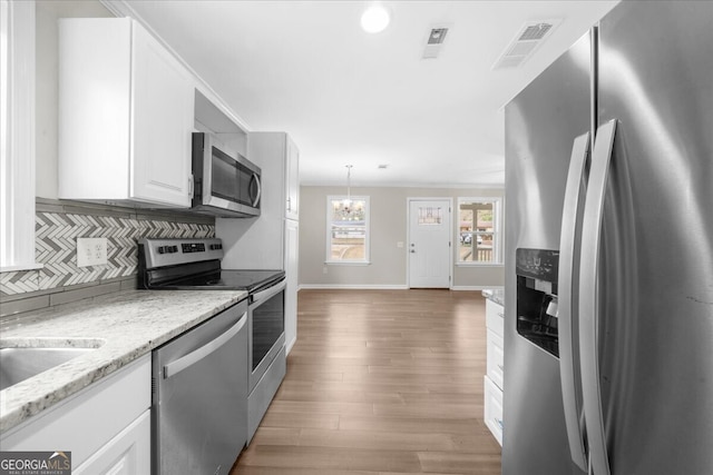 kitchen with appliances with stainless steel finishes, pendant lighting, white cabinets, decorative backsplash, and light stone counters