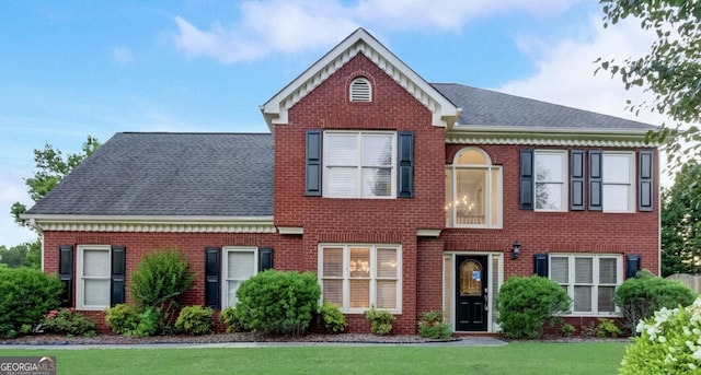 view of front of home featuring brick siding, a front yard, and roof with shingles