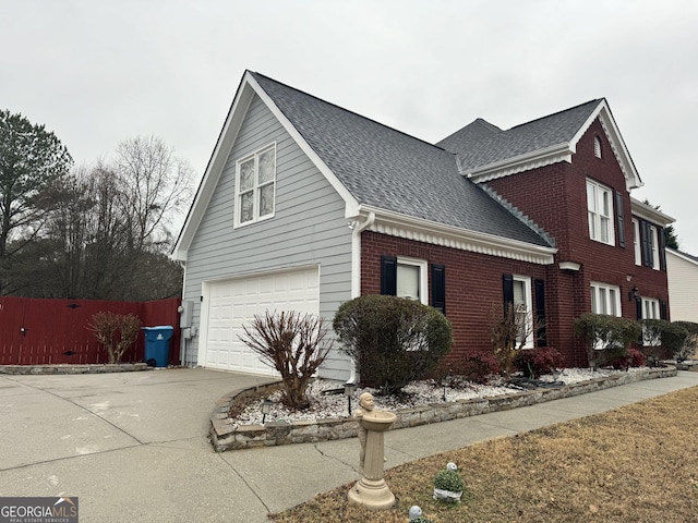 view of home's exterior featuring fence, a shingled roof, brick siding, a garage, and driveway
