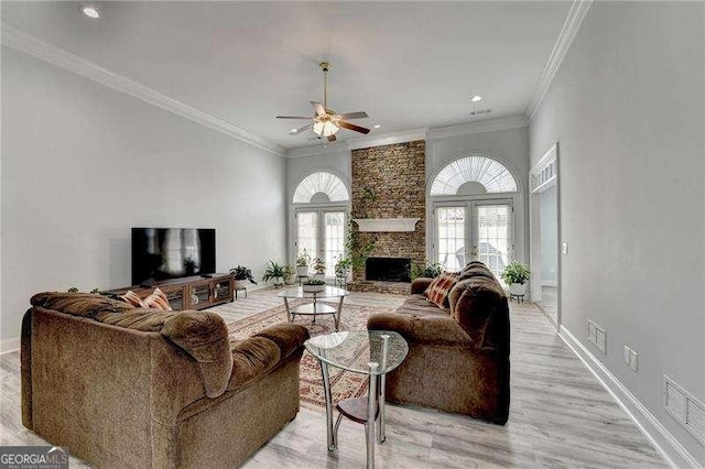 living room featuring crown molding, ceiling fan, a fireplace, light hardwood / wood-style floors, and french doors