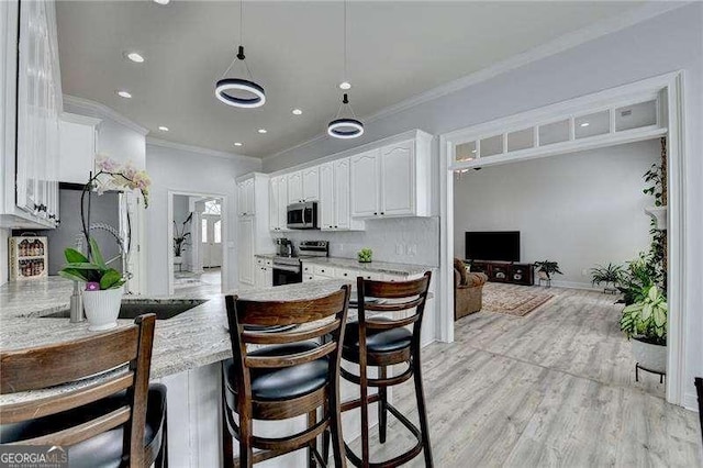 kitchen with white cabinetry, ornamental molding, stainless steel appliances, light stone countertops, and light wood-type flooring