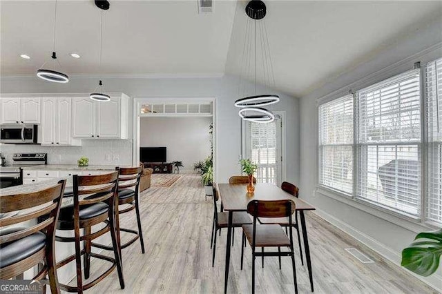 dining space featuring crown molding, lofted ceiling, and light hardwood / wood-style floors