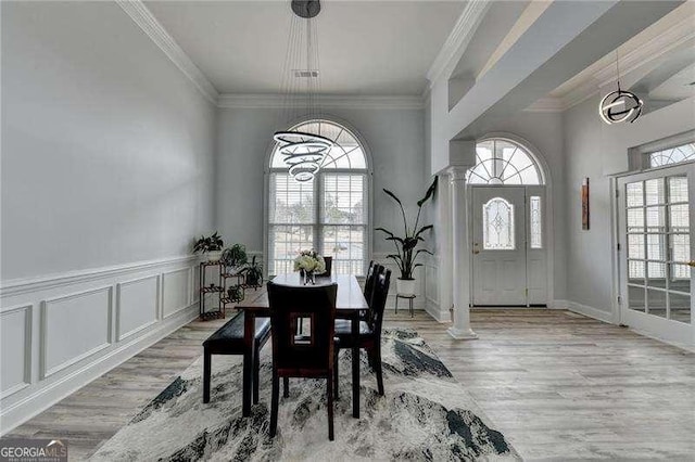 dining area with crown molding, a chandelier, decorative columns, and light hardwood / wood-style flooring