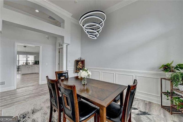 dining area with ornate columns, ornamental molding, an inviting chandelier, and light hardwood / wood-style flooring