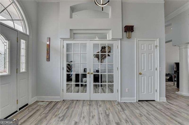 entryway featuring french doors, ornate columns, a towering ceiling, and light wood-type flooring