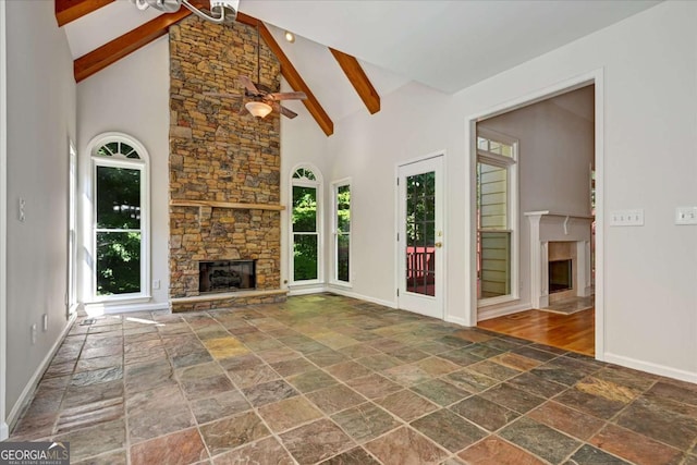 unfurnished living room featuring beamed ceiling, ceiling fan, a stone fireplace, and high vaulted ceiling