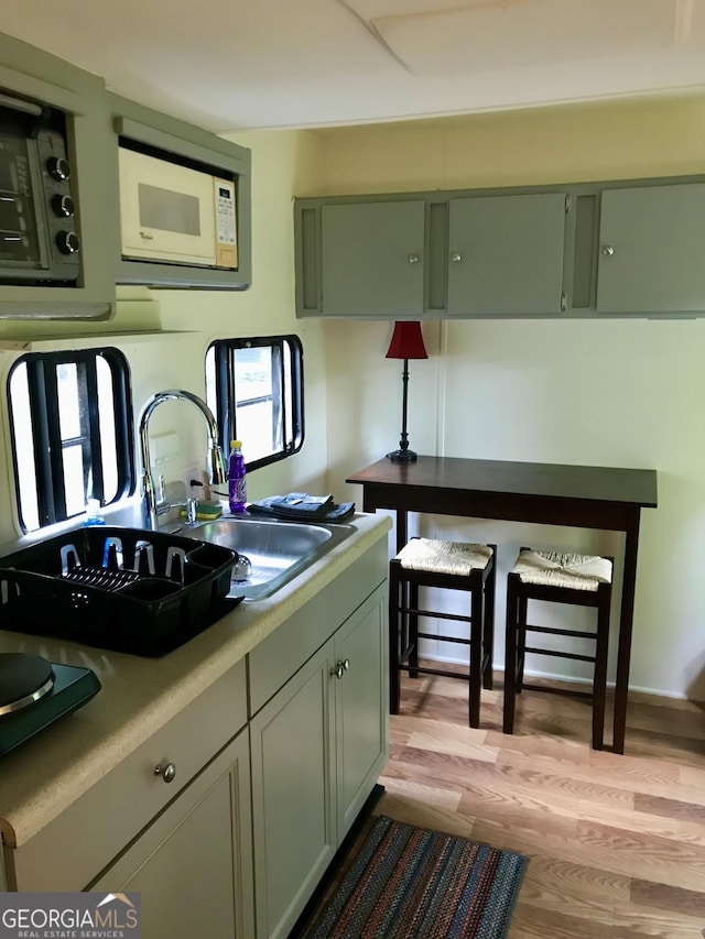 kitchen with sink, green cabinets, white microwave, and light wood-type flooring