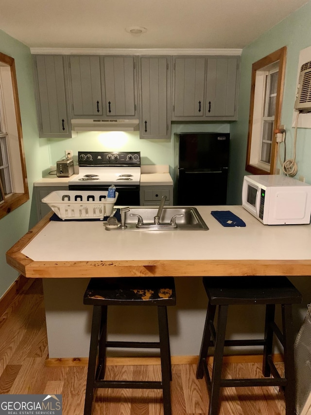 kitchen with sink, black refrigerator, gray cabinetry, electric range, and a kitchen breakfast bar