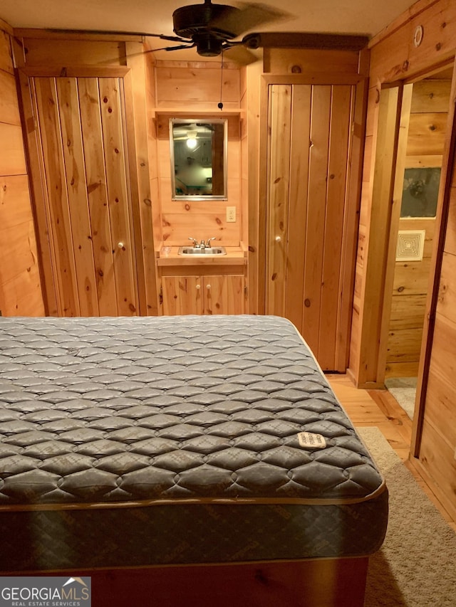 bedroom featuring sink, ensuite bath, hardwood / wood-style floors, and wood walls