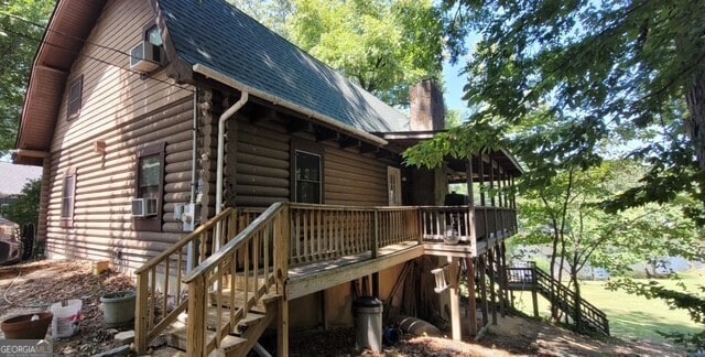 view of side of property with a wooden deck, stairs, roof with shingles, log siding, and a chimney