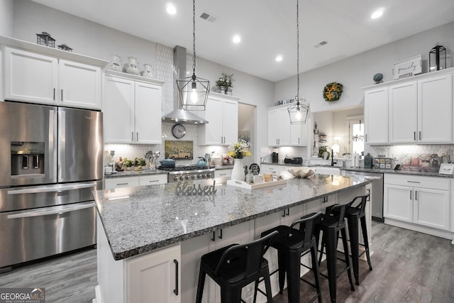 kitchen featuring decorative light fixtures, a center island, appliances with stainless steel finishes, wall chimney range hood, and white cabinets