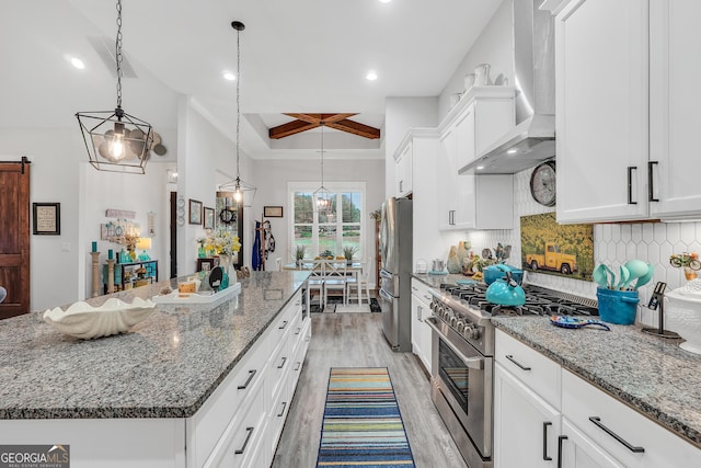 kitchen featuring white cabinetry, appliances with stainless steel finishes, a center island, and wall chimney range hood