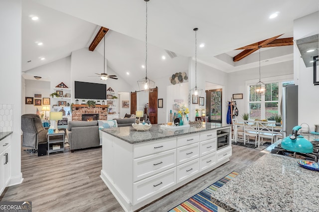 kitchen with light stone counters, a center island, beamed ceiling, a fireplace, and white cabinets