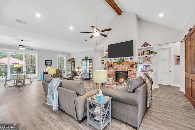 living room featuring beamed ceiling, a barn door, ceiling fan, a brick fireplace, and light hardwood / wood-style flooring