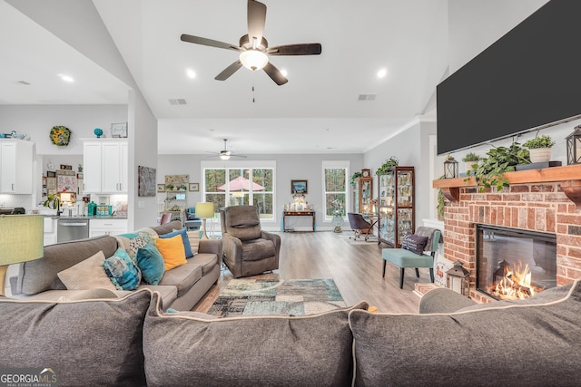 living room featuring ceiling fan, a fireplace, high vaulted ceiling, and light wood-type flooring