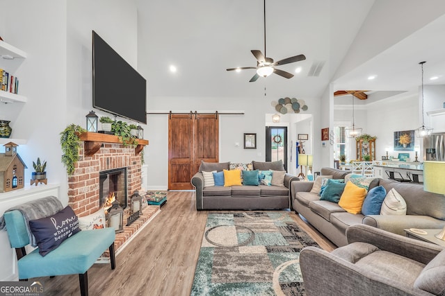 living room featuring high vaulted ceiling, a fireplace, ceiling fan, light hardwood / wood-style floors, and a barn door