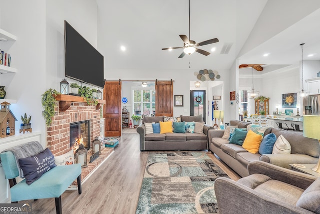 living room with ceiling fan, a barn door, high vaulted ceiling, and light hardwood / wood-style floors