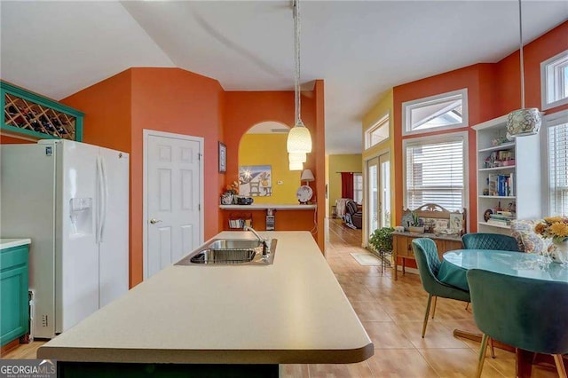 kitchen with light tile patterned flooring, sink, decorative light fixtures, white refrigerator with ice dispenser, and a kitchen island with sink